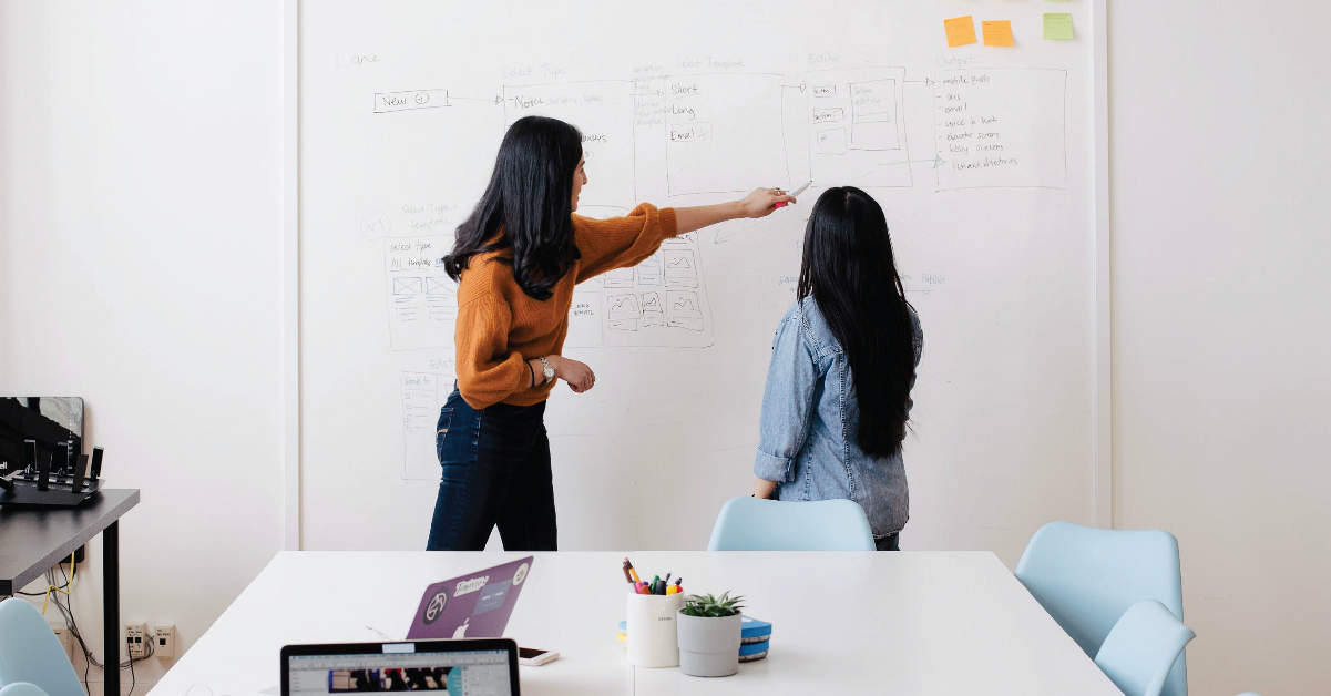 two women drawing on a white board
