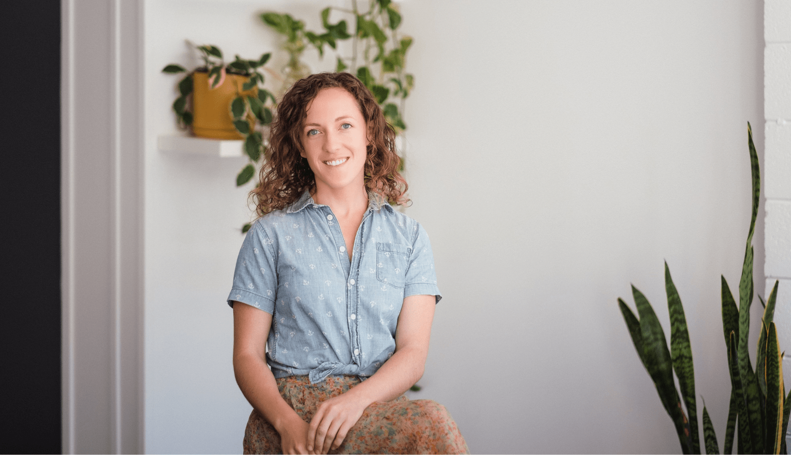 Hannah Sabih. Professional image of Lemon Tree's Digital Lead sitting in front of white wall and plants.