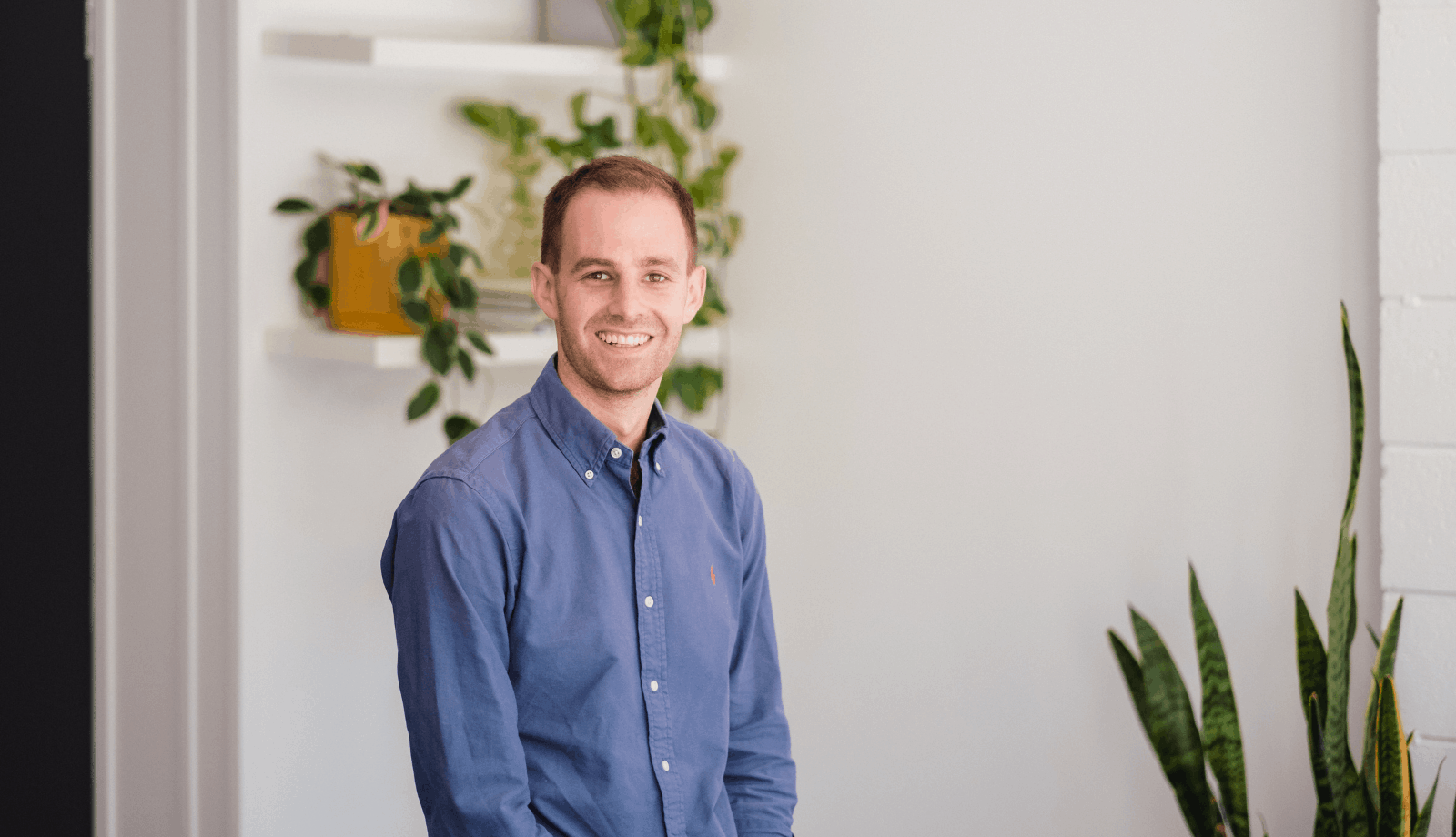 Lemon TrSocial Advertising Specialist, Josh in a blue button up shirt, sitting on a stool smiling at the camera.