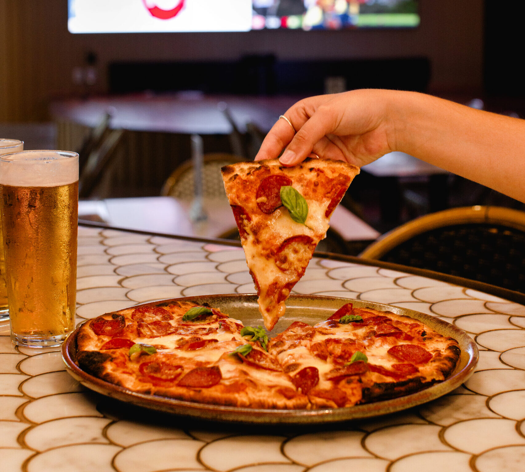 close up image of a pizza and beer. a hand is removing a slice of pizza from the tray